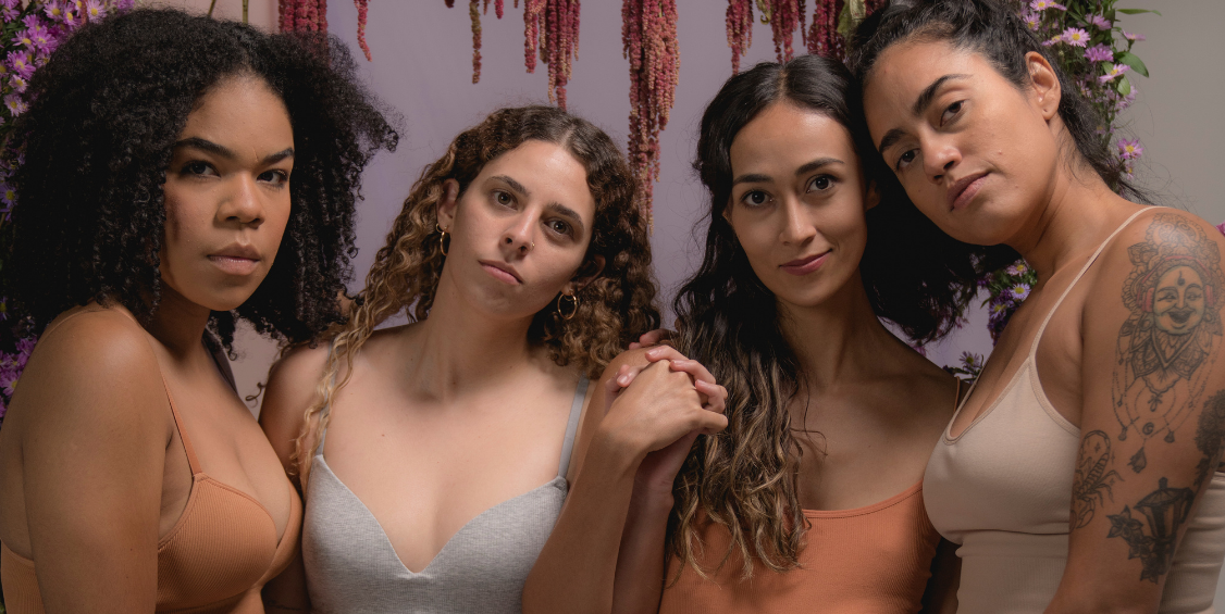 Four women posing together in matching nude-toned lingerie sets, with a floral hanging backdrop and the text 'Blush Boudoir' and 'ALL ABOUT THE BRAND' framing the photo.